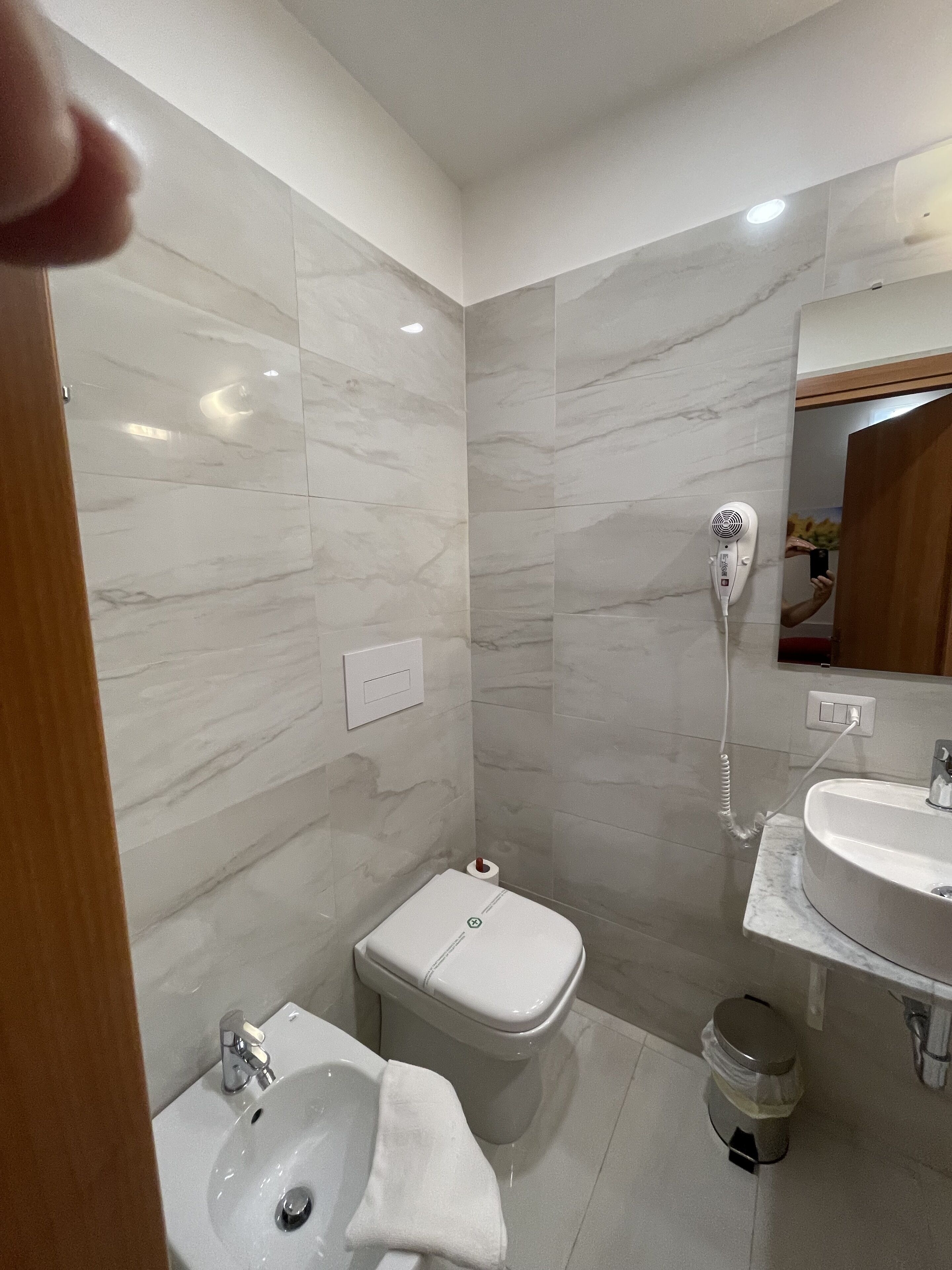 Un baño moderno con inodoro, bidé, lavamanos y un secador de pelo fijado en la pared.