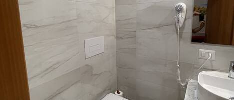 Un baño moderno con inodoro, bidé, lavamanos y un secador de pelo fijado en la pared.