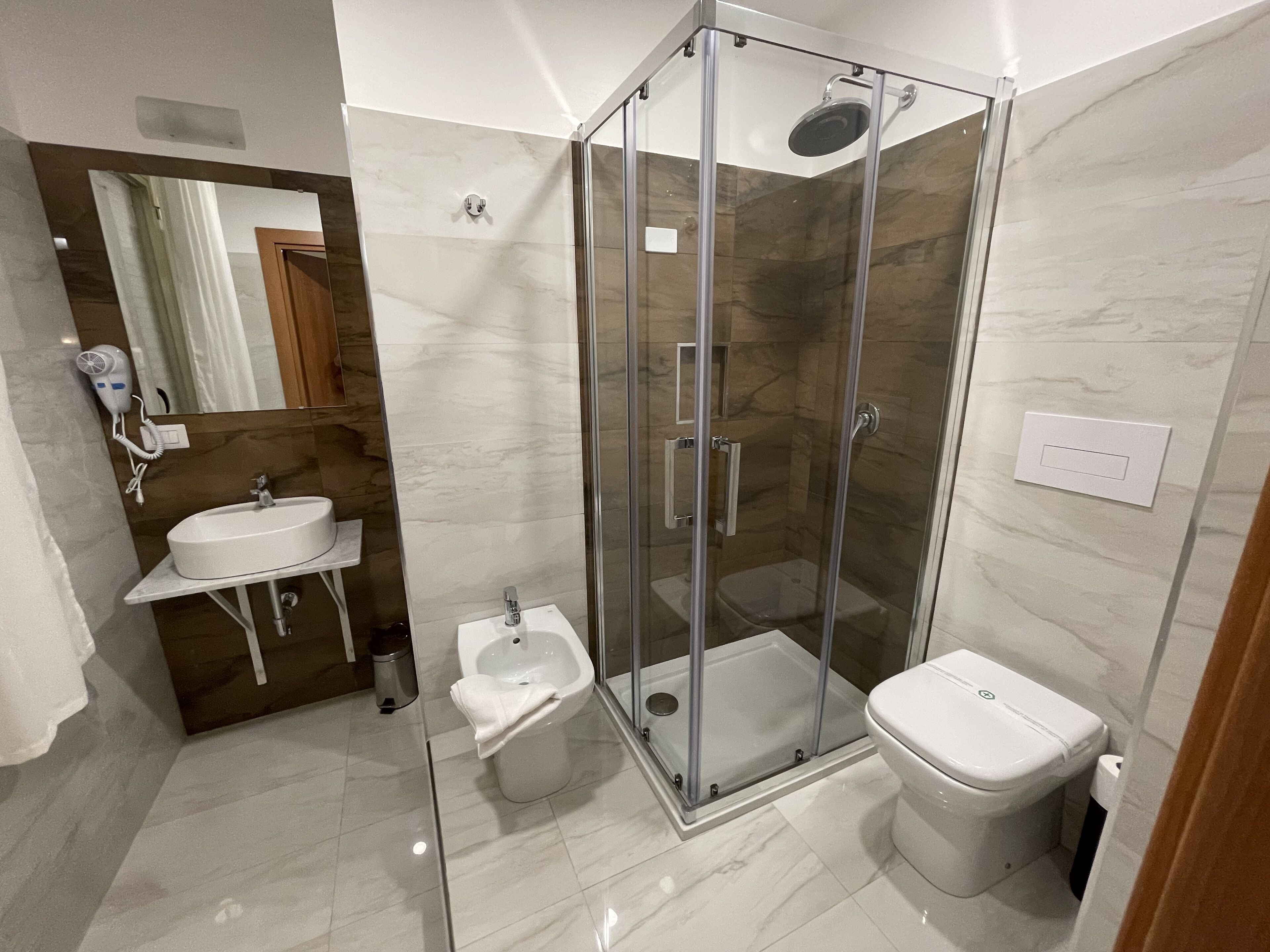 Un baño moderno con ducha de vidrio, lavamanos pedestal y inodoro.