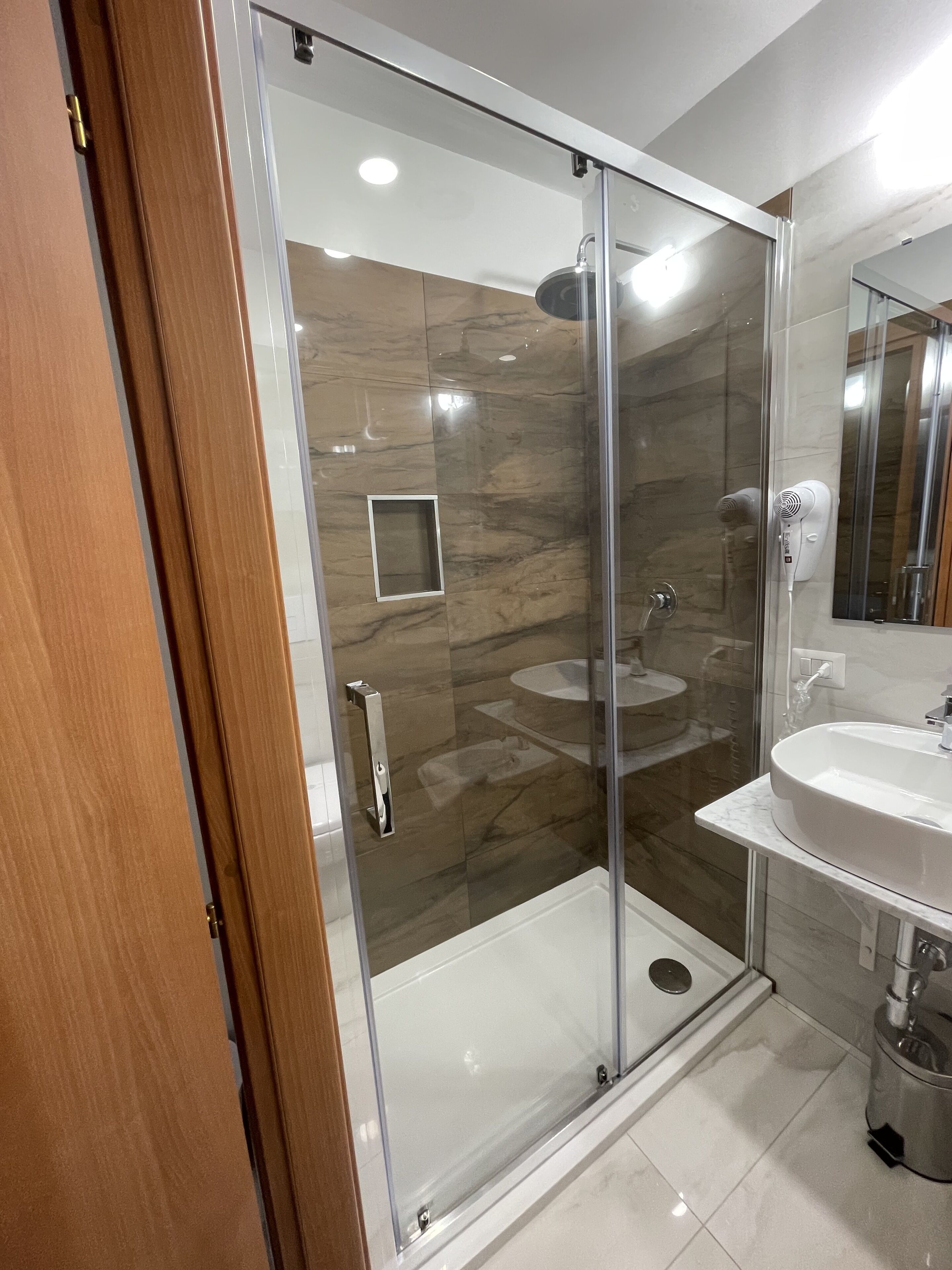A modern bathroom with a glass-enclosed shower, a marble-tiled floor, and a white sink with a mirror above it.