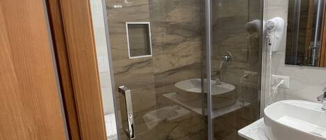 A modern bathroom with a glass-enclosed shower, a marble-tiled floor, and a white sink with a mirror above it.