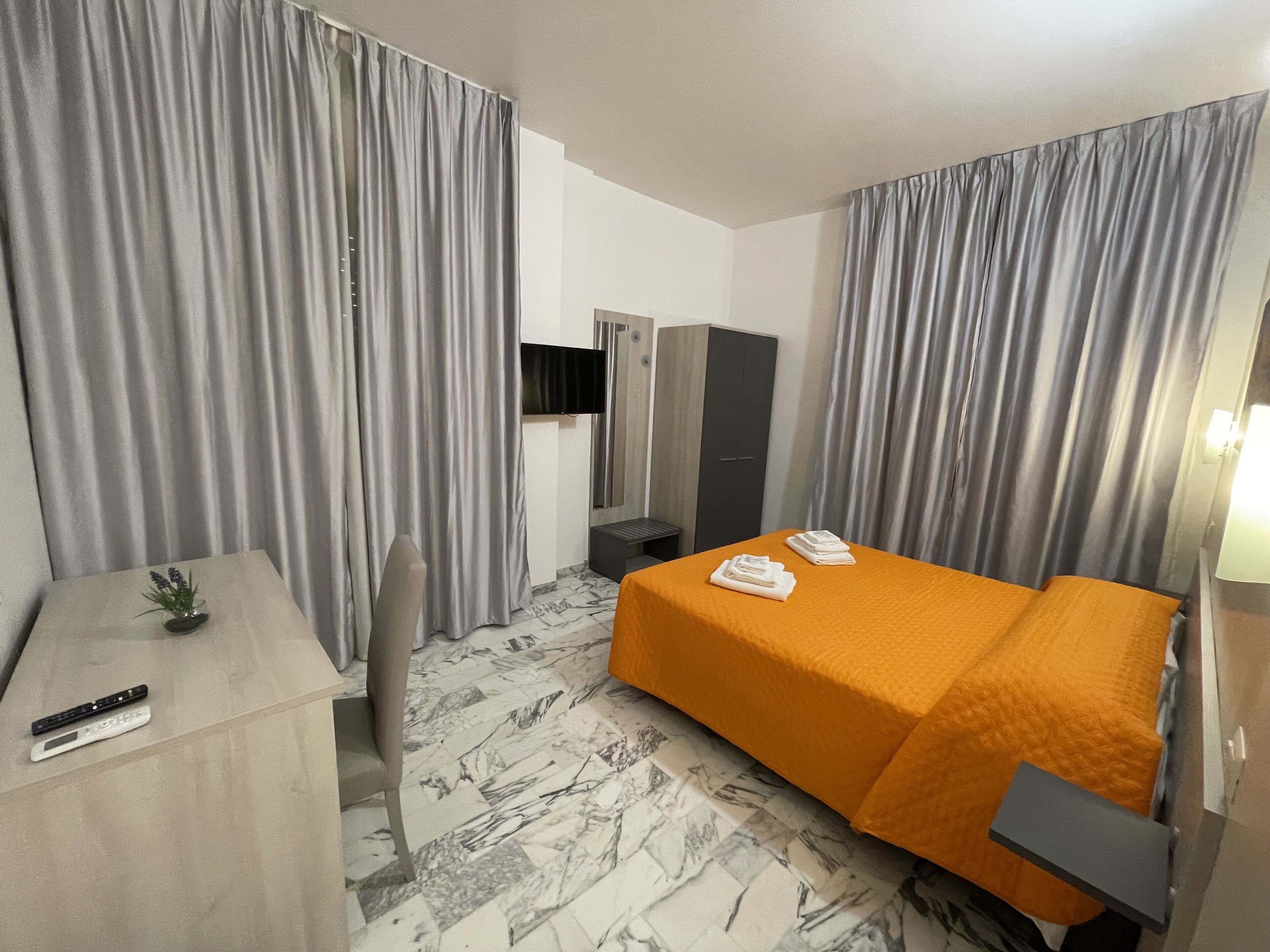 Una habitación de hotel con cama, escritorio, televisor y armario.