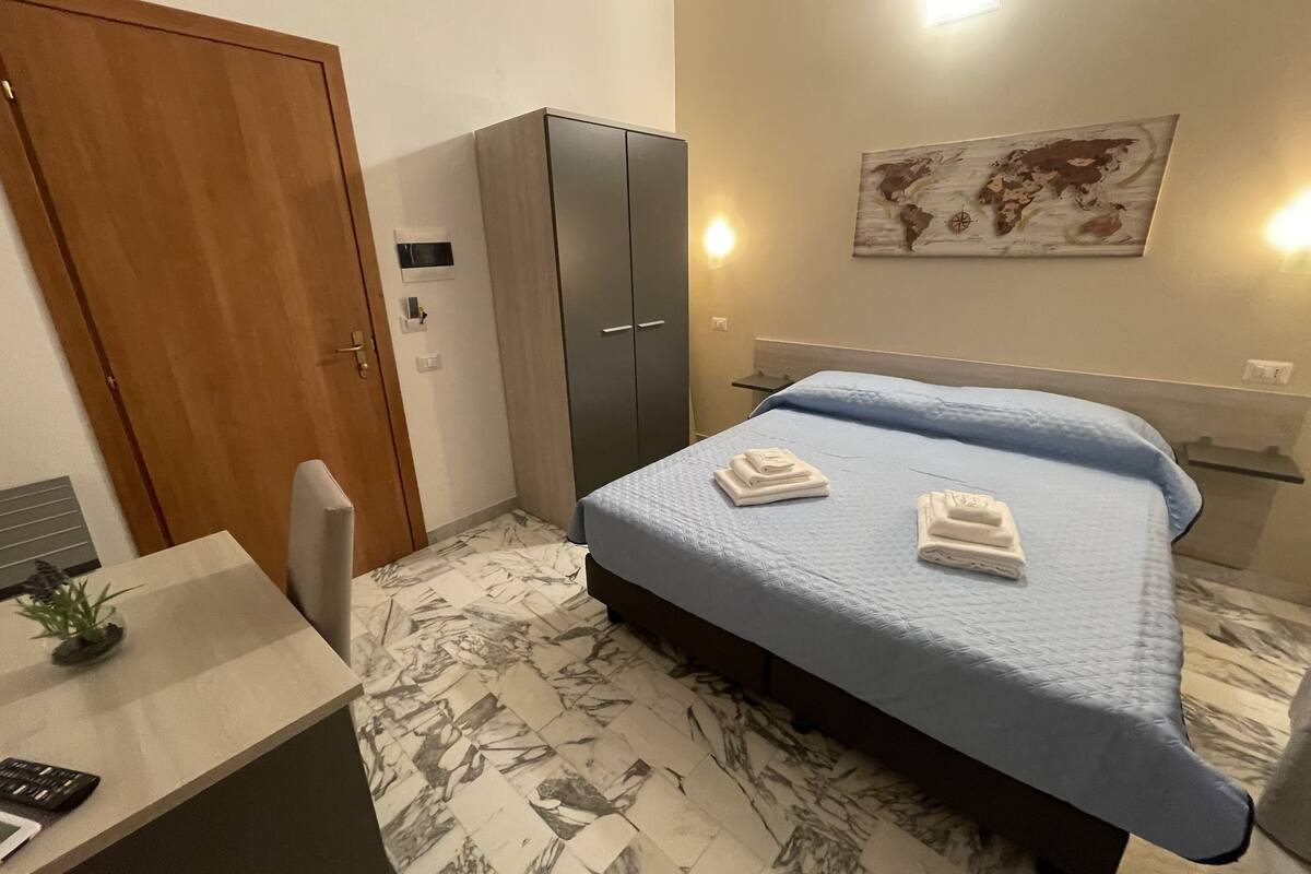 Una habitación de hotel con cama, escritorio, armario y un mapa mundial en la pared.