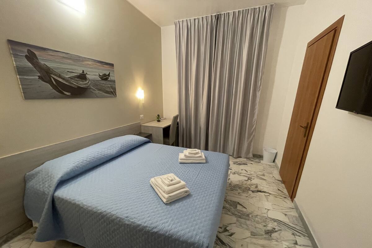 Habitación de hotel con cama, escritorio, silla, televisor y un cuadro en la pared.