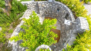 Tinaco de hidromasaje al aire libre construido con piedra, rodeado de exuberante vegetación y un muro de piedra.