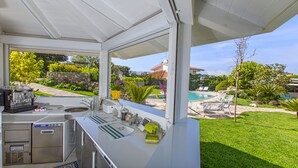 Cocina exterior con vistas a una piscina y jardín.