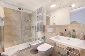 A modern bathroom with a glass-enclosed shower, a bidet, a toilet, and a sink with toiletries.