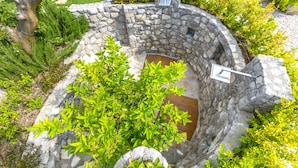 Un bain à remous extérieur en pierre, entouré d’une végétation luxuriante et bordé d’un mur de pierre.