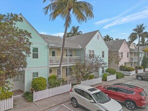 Houses with traditional architecture and balconies are surrounded by a white picket fence and lush greenery.