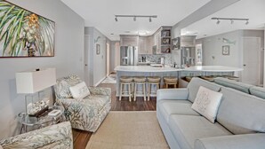A modern kitchen with a central island, bar stools, and a dining area with a light blue sofa and patterned armchairs. - A Fish Bowl at The Truman Annex in Key West (Key West)