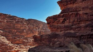 Paesaggio desertico con imponenti scogliere di arenaria rossa e un primo piano sabbioso.