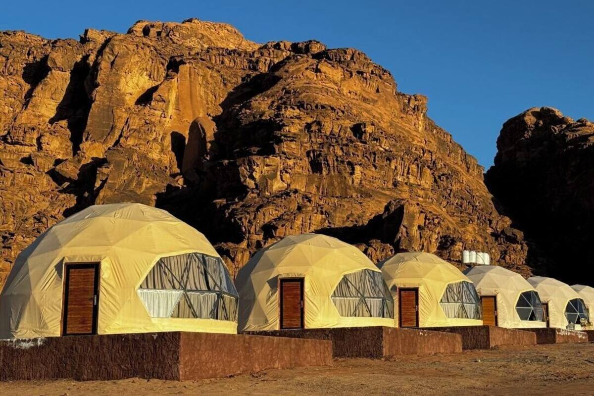 A row of dome-shaped tents with wooden doors, set against a rocky cliff backdrop.