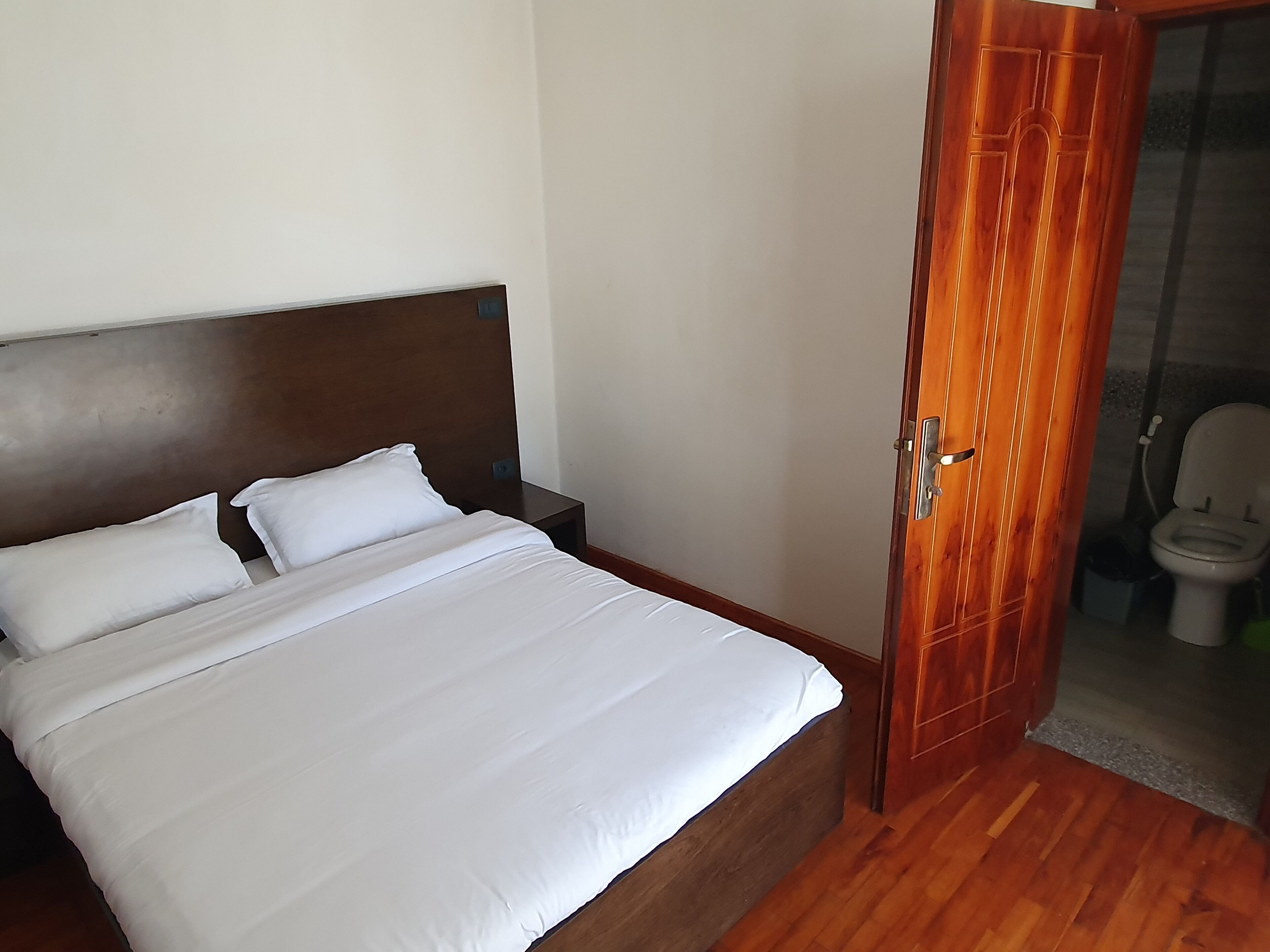 Un letto rifatto con lenzuola bianche in una stanza con pavimento in legno e una porta di legno.