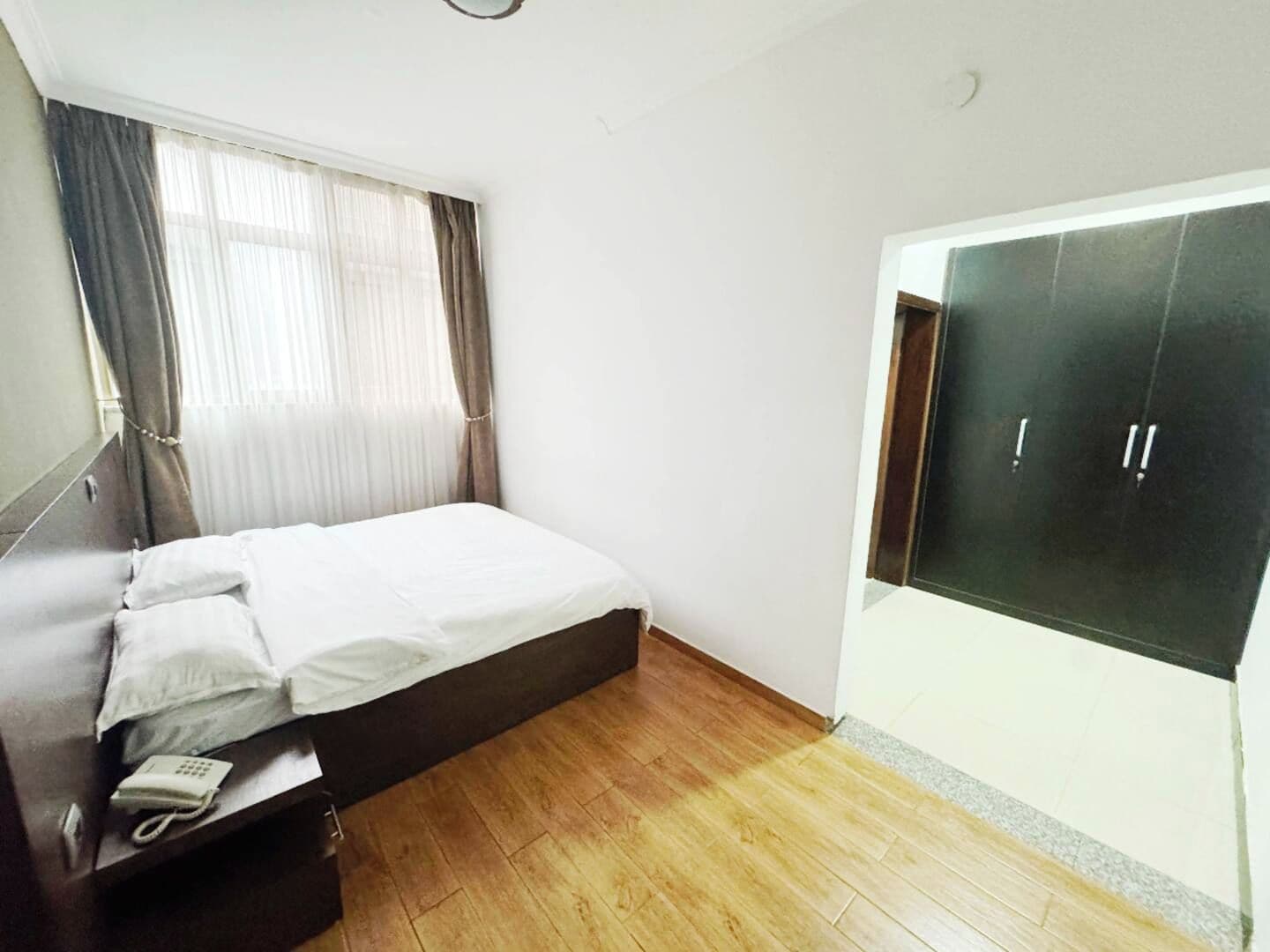 A bedroom with a bed, a telephone, a wardrobe, and a window with curtains.