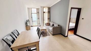 A modern living room with a dining area, a sofa, and a bed in the background.