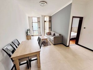 A modern living room with a dining area, a sofa, and a bed in the background.