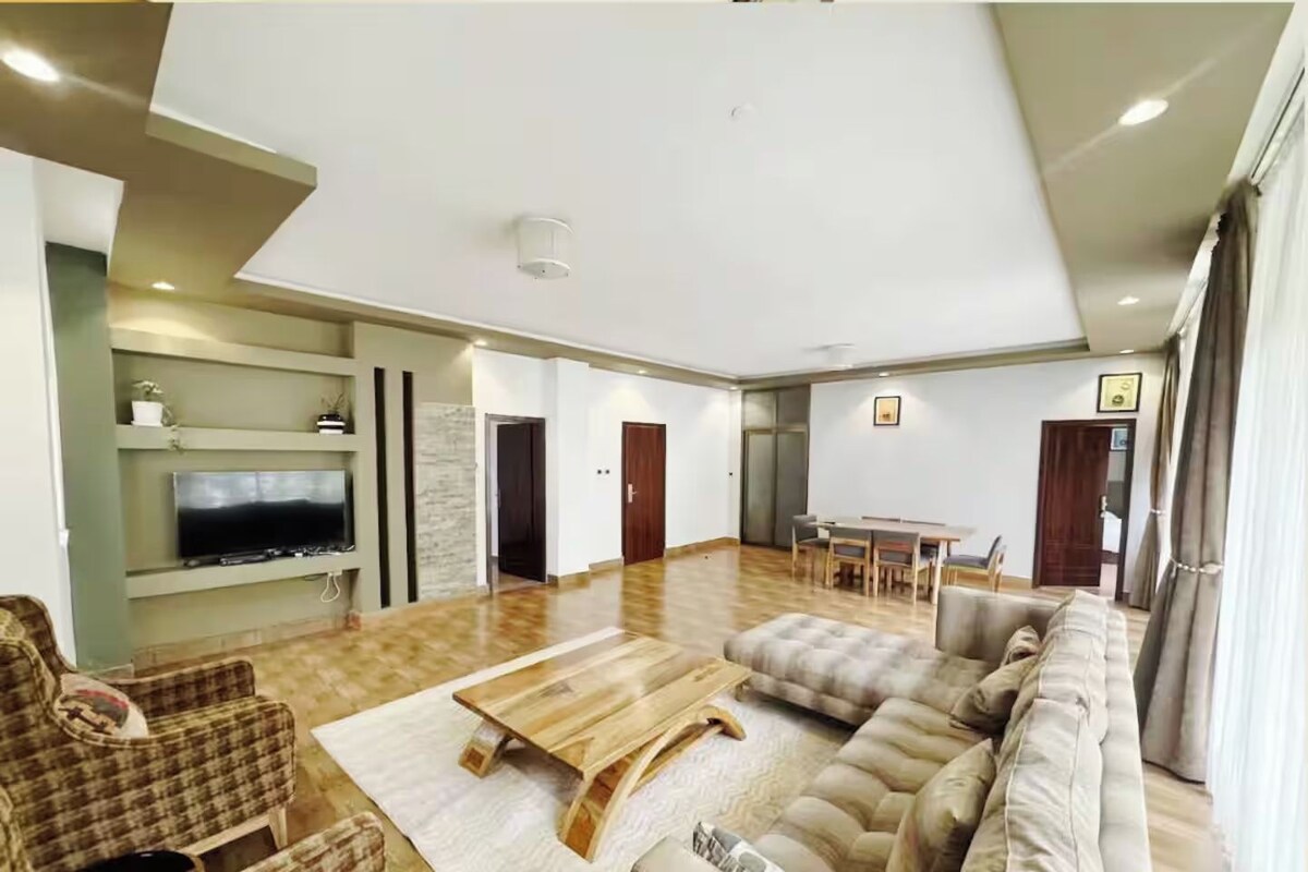 Un salon spacieux, doté d’un grand canapé, d’une table basse en bois et d’un téléviseur à écran plat fixé au mur.