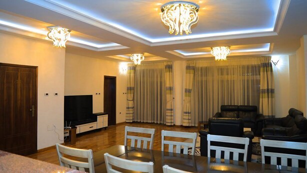 A spacious living room with a flat-screen TV, a dining table with chairs, a sofa set, and decorative lighting fixtures. - Rankset Guesthouse apartment (Addis Ababa)