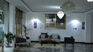 A modern living room with a marble floor, a chandelier, two sofas, a coffee table, and wall-mounted lights. - Rankset Guesthouse apartment (Addis Ababa)