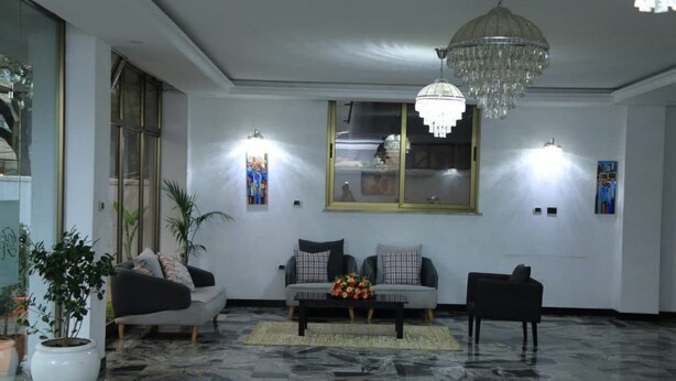 Una sala de estar moderna con piso de mármol, una araña, dos sofás, una mesa de centro y luces fijadas a la pared.