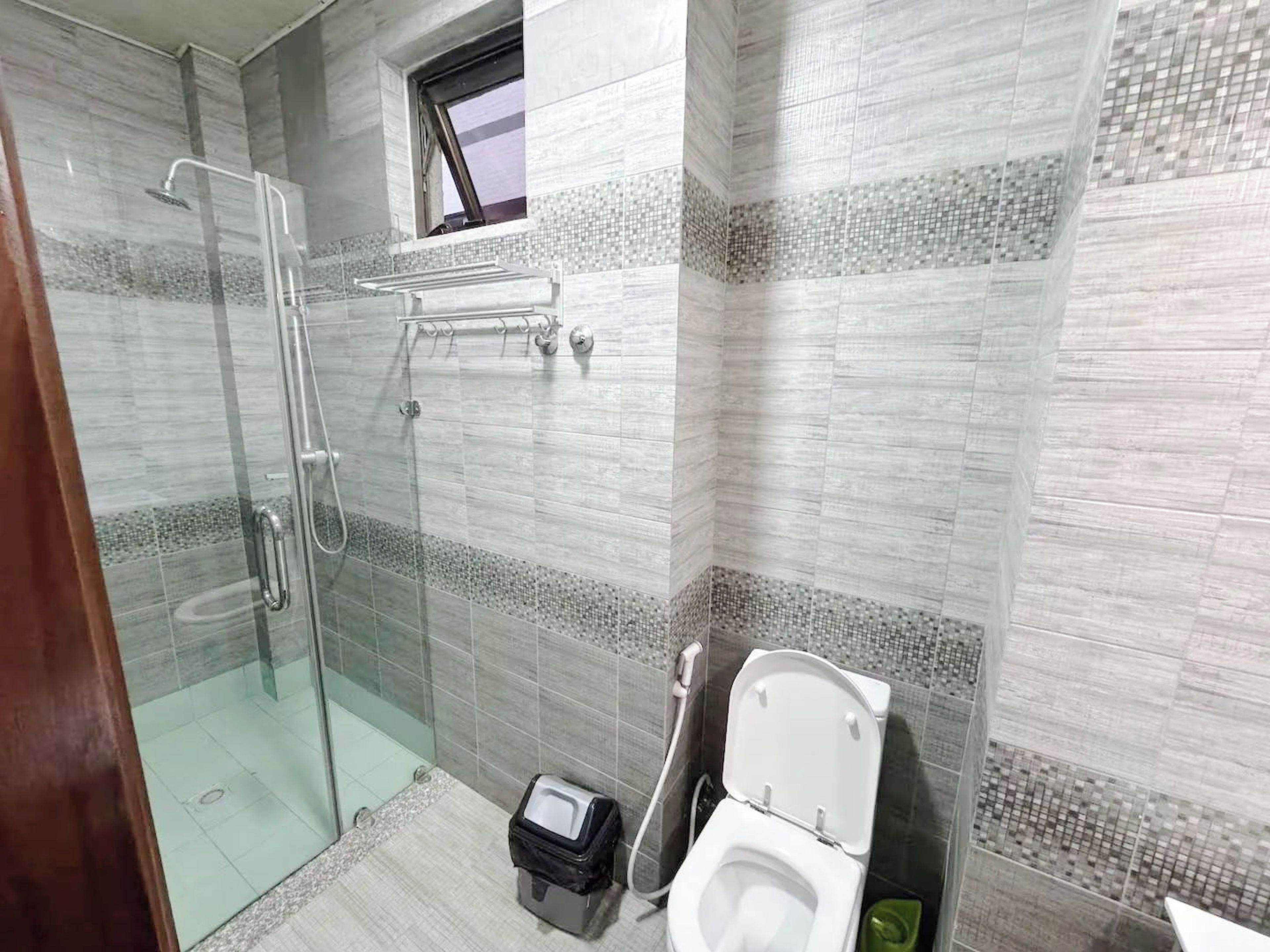 Une salle de bain avec une douche à parois de verre, des toilettes et une petite fenêtre.