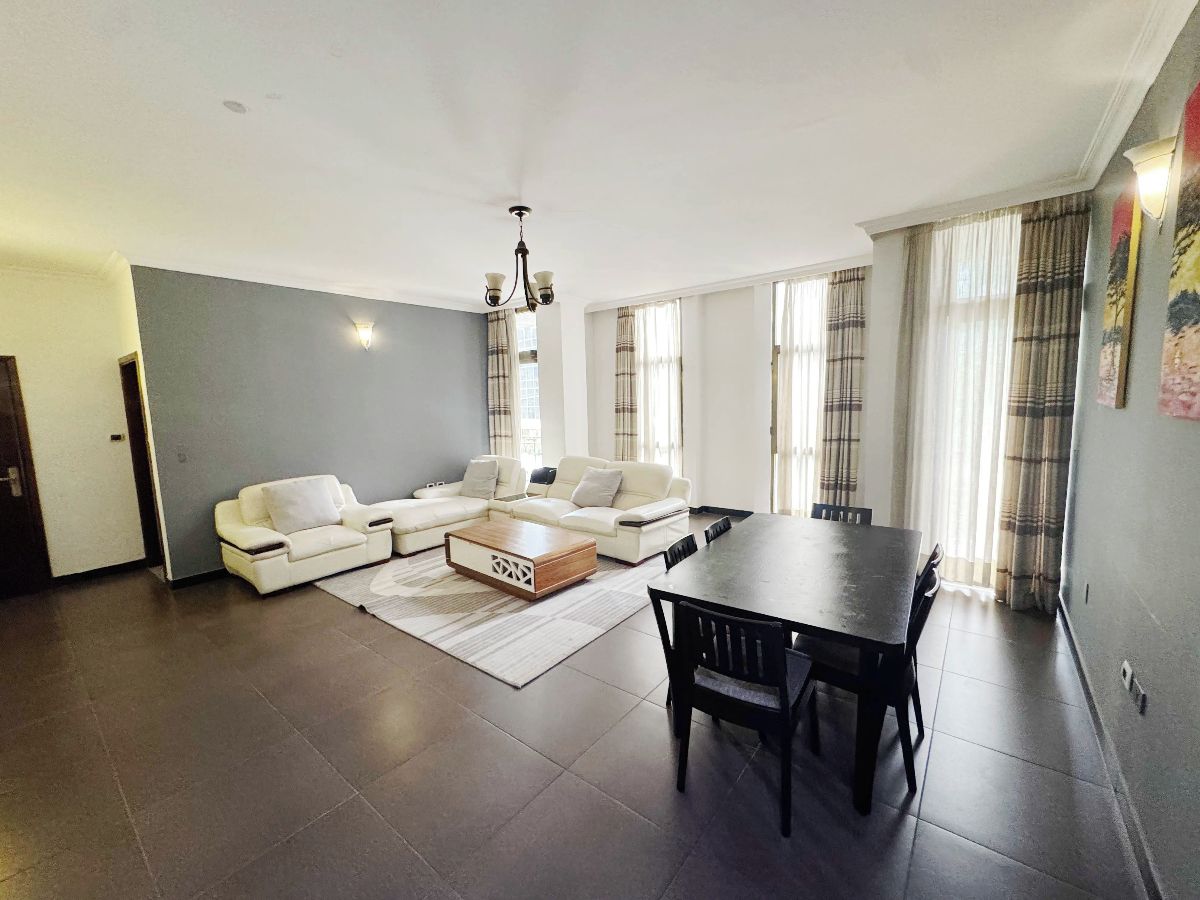 A spacious living room with a sectional sofa, a dining table, and a chandelier.