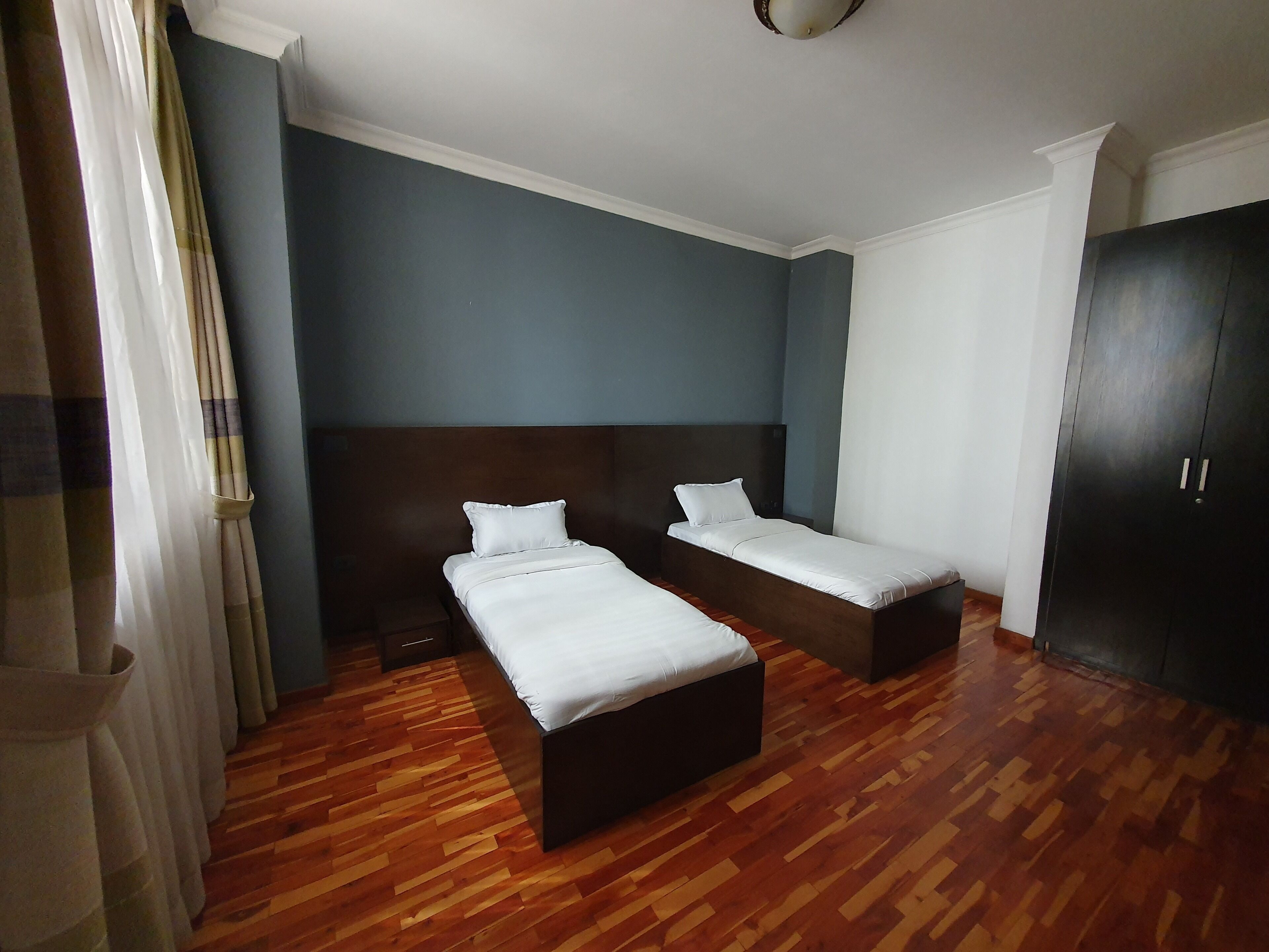 Une chambre d’hôtel avec deux lits, un plancher en bois et une armoire sombre.