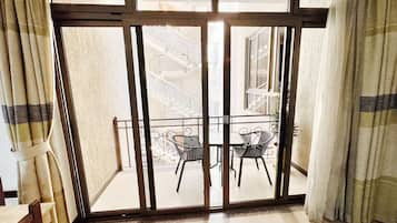 Een kamer met een schuifdeur die leidt naar een balkon met twee stoelen en een tafel.