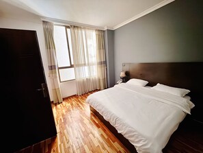 Et hotelværelse med en stor seng, et natbord med lampe, et klædeskab og et vindue med gardiner.