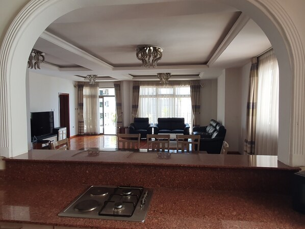 A spacious living area with a kitchen island, a flat-screen TV, a sofa, and a dining table.
