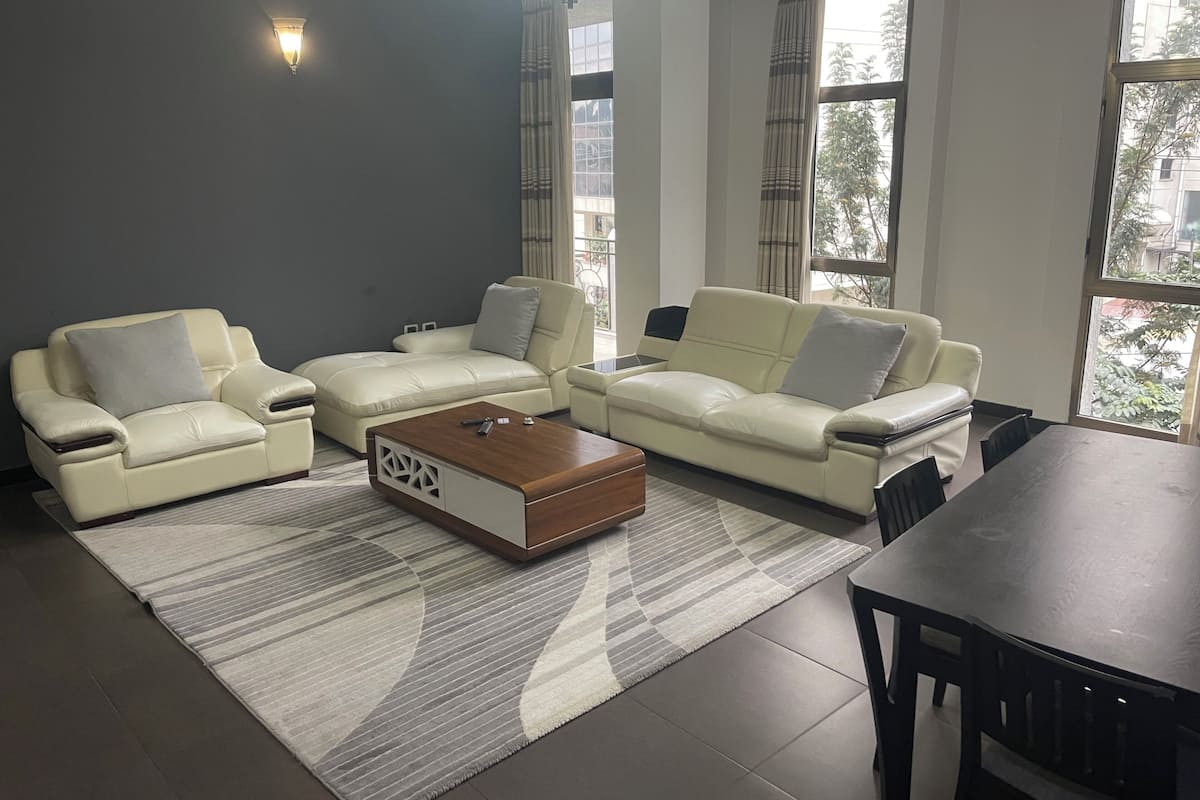 A modern living room with two cream-colored sofas, a wooden coffee table, and a dining table with chairs.
