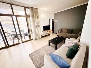 Un salon moderne comprenant un canapé, une table basse, un téléviseur et une porte-fenêtre coulissante donnant sur un espace extérieur avec une table et des chaises.