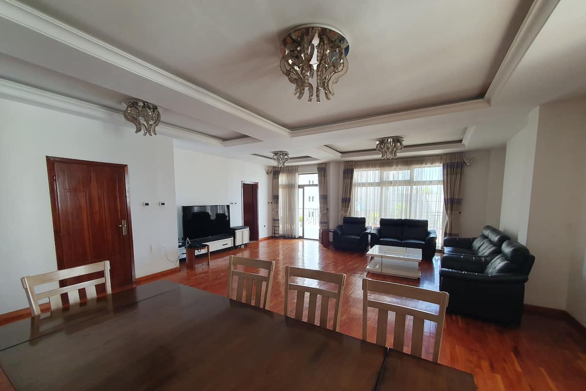 A spacious living room with a large wooden dining table, two black sofas, and a flat-screen TV.