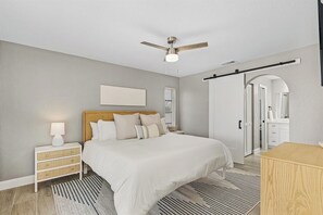 A bedroom with a bed, bedside tables, a ceiling fan, a window, and a door. - VRCC Villa White Palm (Cape Coral)