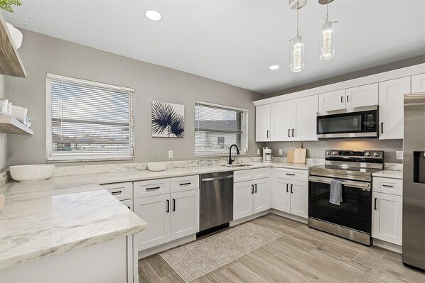 A modern kitchen with white cabinets, stainless steel appliances, and a marble countertop.