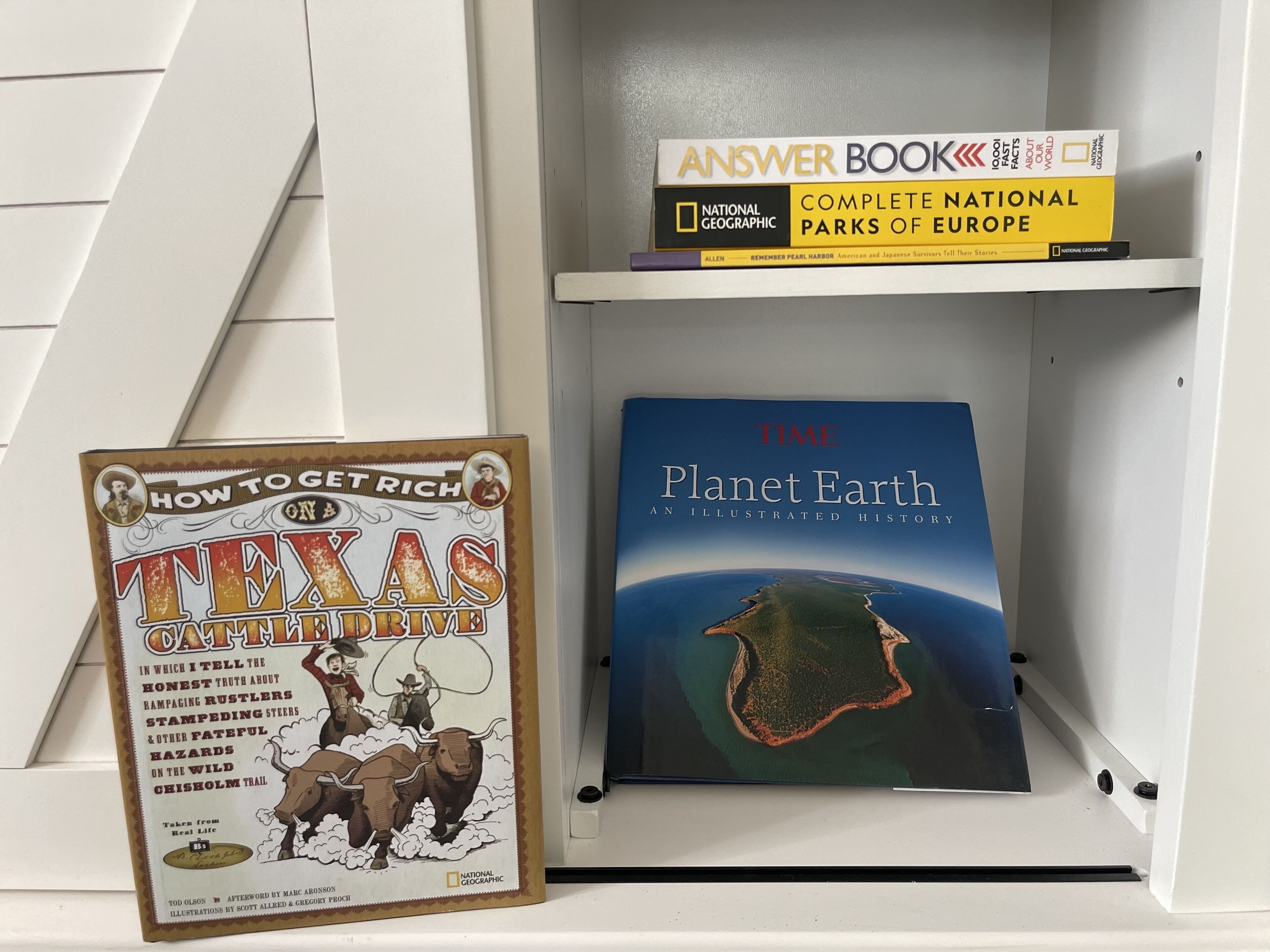 Une bibliothèque contenant des livres tels que « Texas Cattle Drive », « Planet Earth » et « Complete National Parks of Europe ».