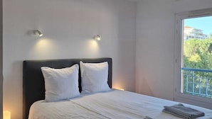 A bedroom with a bed, two wall-mounted lights, a nightstand, and a window with a view of greenery.