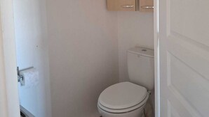 A small, clean bathroom with a toilet, a cabinet above it, and a roll of toilet paper on the wall.