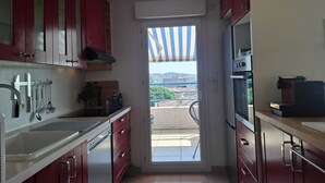 A compact kitchen with red cabinets, a built-in dishwasher, and a view through a sliding glass door to an outdoor terrace.