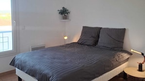 A bedroom with a bed, a bedside lamp, a small table, and a potted plant.