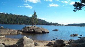 A rocky shoreline with a clear view of a forested hill in the background. - Lay-Z-Bones ~ AC & Pool Access! (Dorrington)