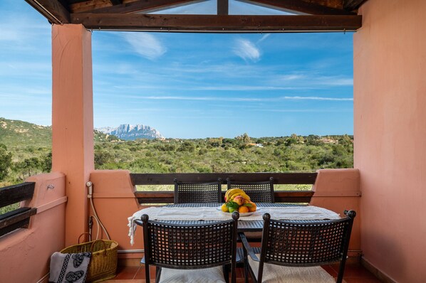 A balcony with a table set for two, overlooking a mountainous landscape.
