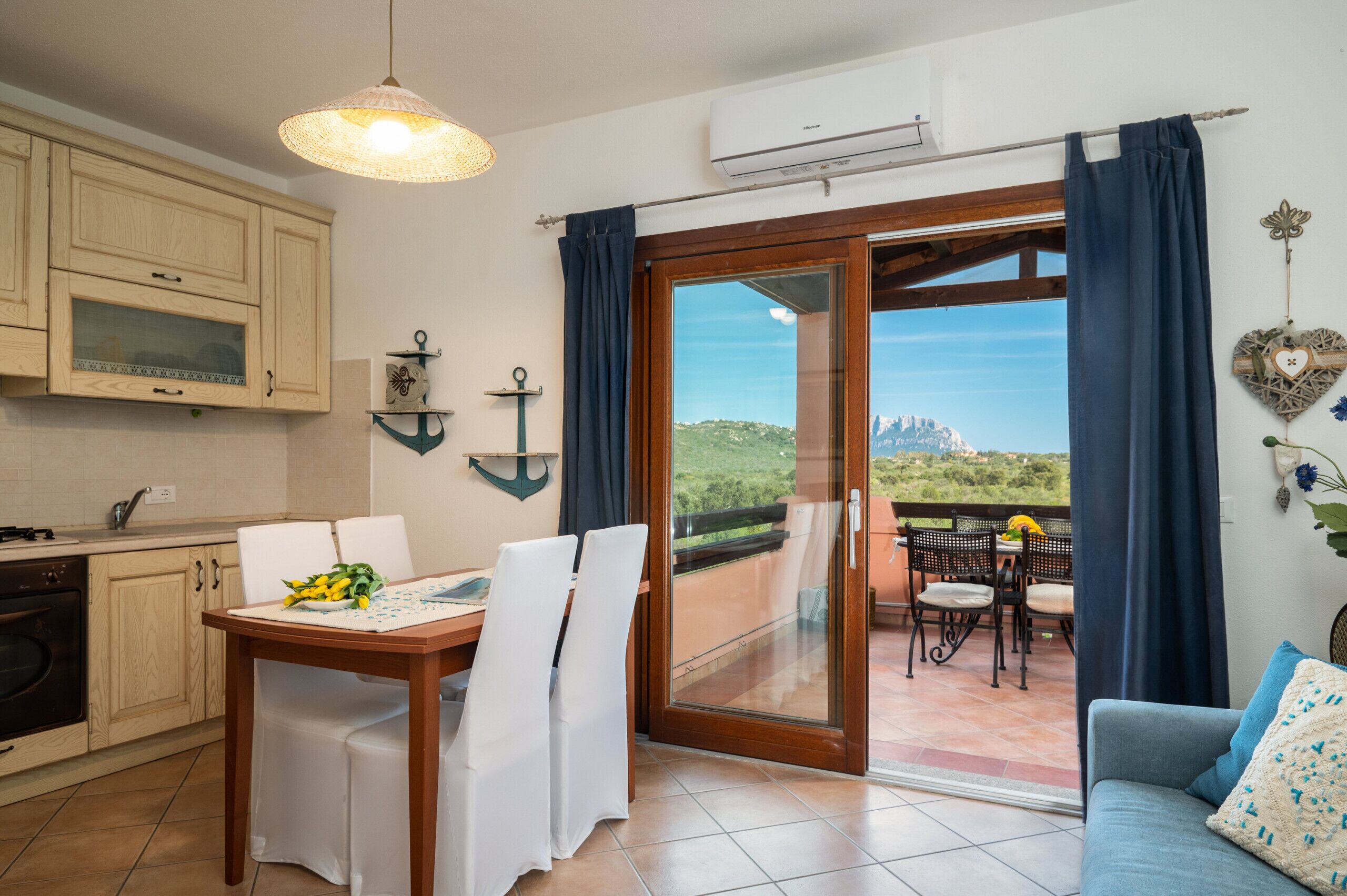 A kitchen with wooden cabinets, a dining table with chairs, and a view of a balcony with a table and chairs.
