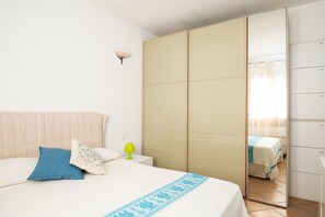 A bedroom with a bed, a bedside table, a lamp, a wardrobe, and a mirror.