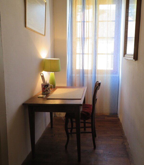 Una habitación pequeña con una mesa de madera, una silla, una lámpara y una ventana con cortinas.