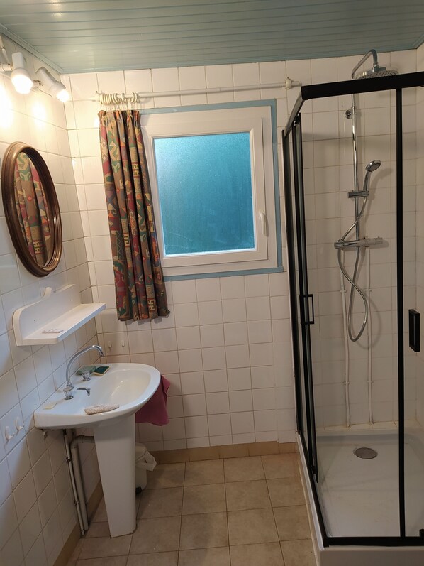 Un baño con un lavamanos blanco, un espejo, una ducha con puerta de vidrio y una ventana con vistas azules.