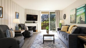 Een moderne woonkamer met een bank, fauteuils, een salontafel, een flatscreen televisie en een open haard.