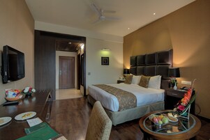 A hotel room with a bed, a dining table, a TV, and a small table with a vase of flowers.