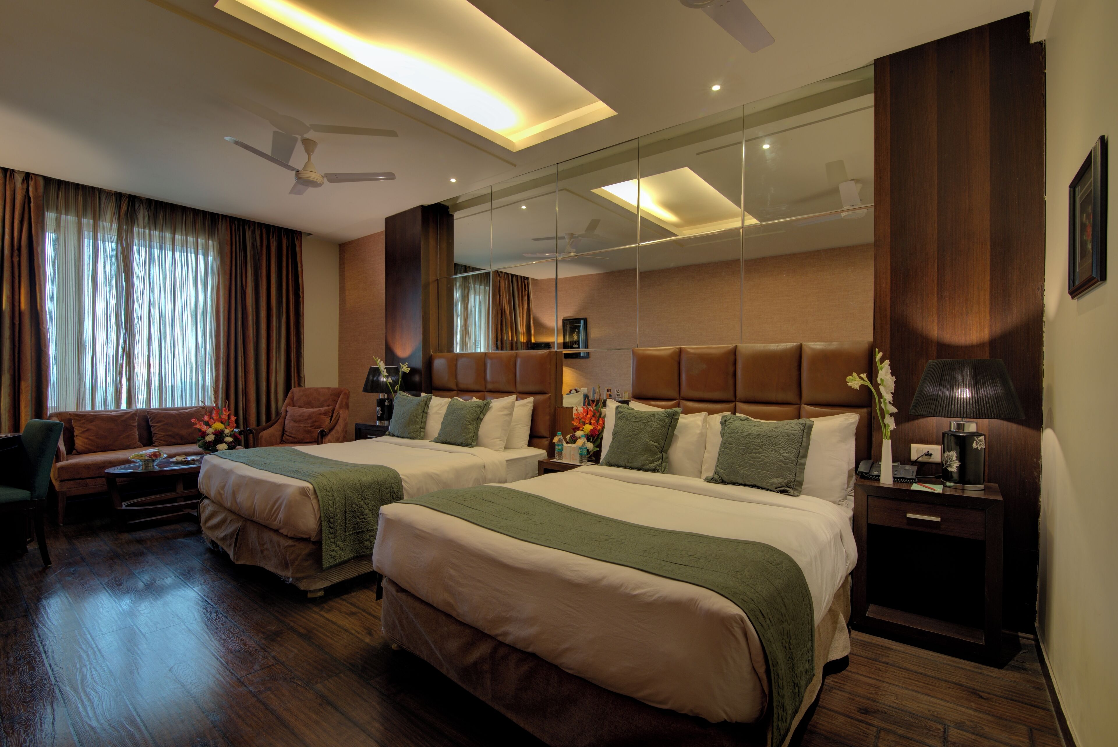 A hotel room with two beds, a sofa, a desk, and a mirror.