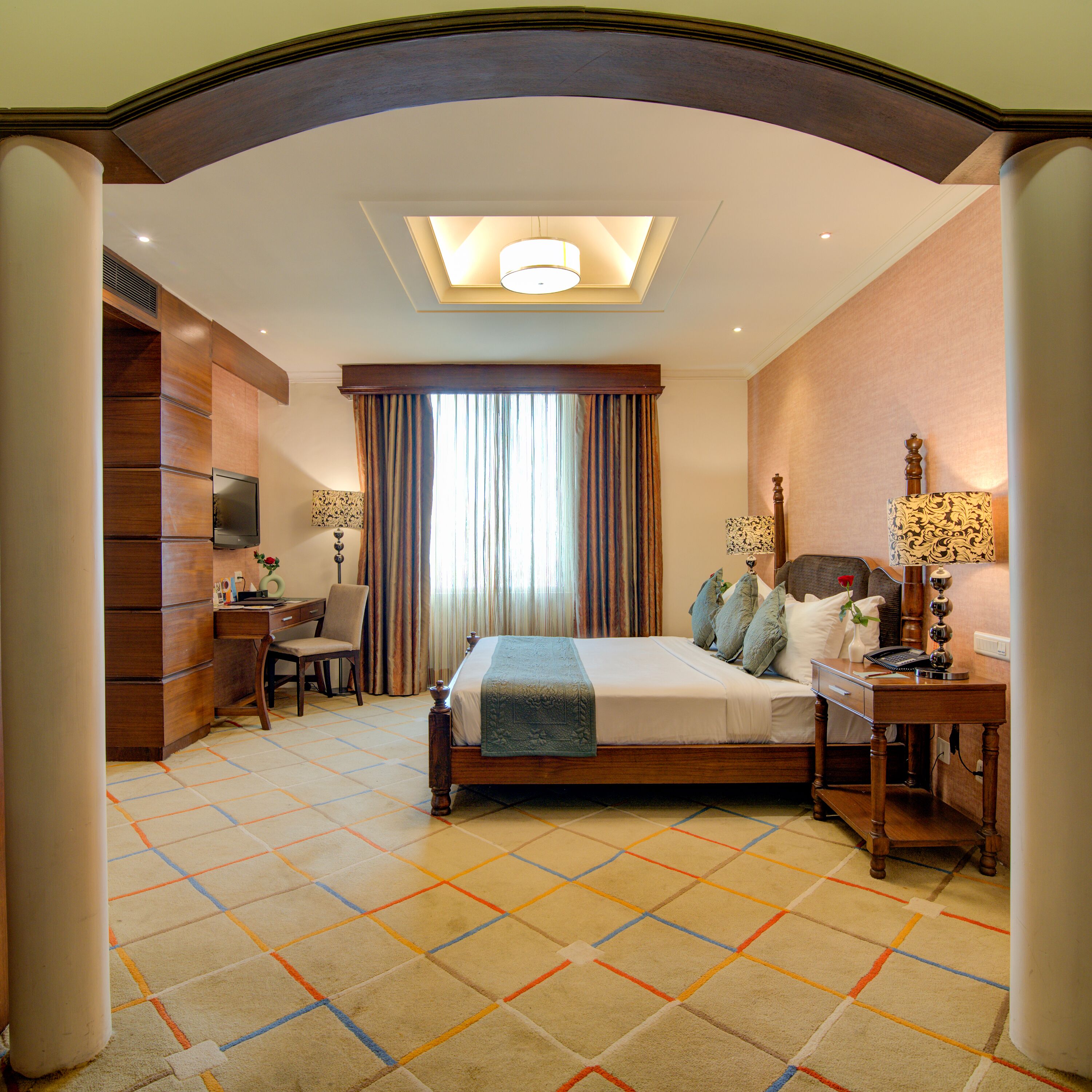A hotel room with a large bed, a desk, a chair, a TV, and a window with curtains.